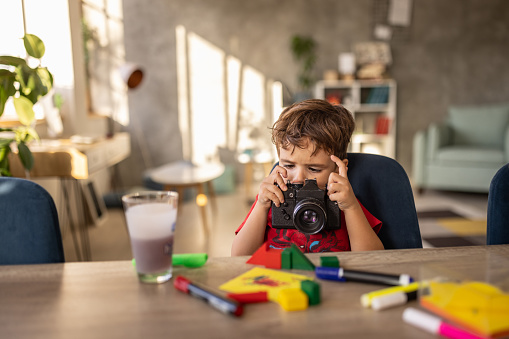 Cute little boy playing with old camera while sitting at the table at home.
