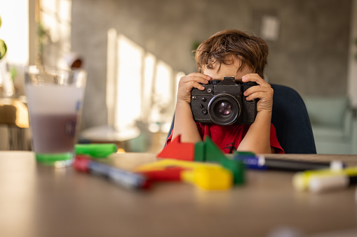 Cute little boy playing with old camera while sitting at the table at home.