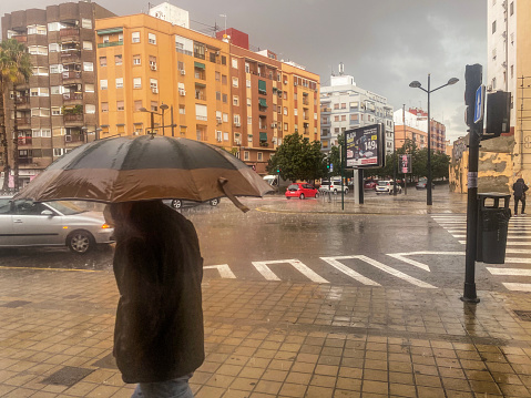 Valencia, Spain - November 27, 2020: Man with umbrella walking in the street under heavy rain. The rainy season can be really hard with a lot of water falling causing even floods all over the province