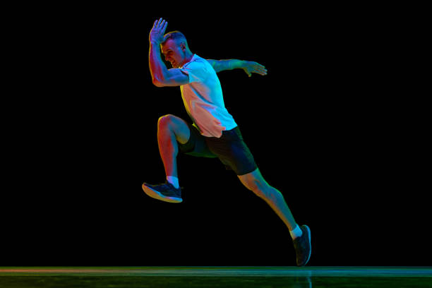 istock Dynamic image of young man with muscular, strong, fit body, professional runner in motion against black studio background in neon light 1500024924