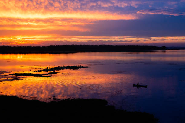 Silhouette of a lonely fisherman in lake during orange sunset over horizon