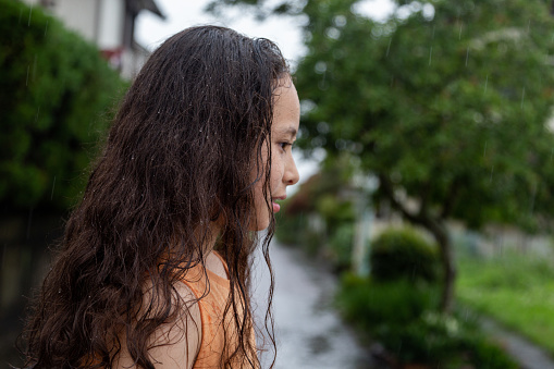 Close-up of teen or child looking profile in rain with wet curly hair. Focus on the wet hair.