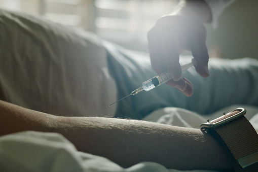 Hand of male doctor of mental hospital holding syringe with liquid medicament while making injection to sleeping patient
