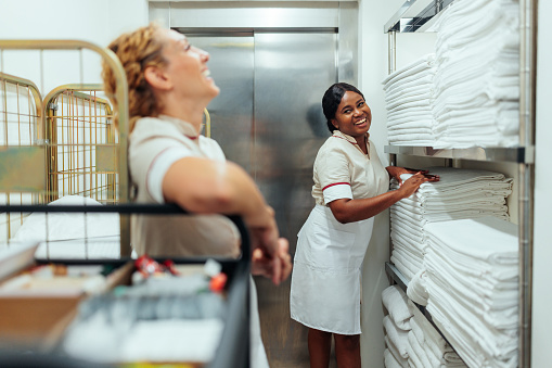 Two interracial hotel maids in white uniforms having a fun conversation in the laundry