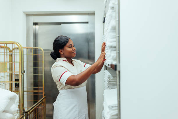 African-American uniformed maid taking clean sheets from shelf