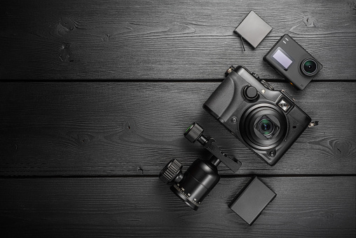 Digital compact and action cameras and equipment on black wooden plank table. Top view, flat lay, copy space.