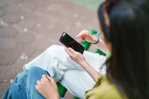 istock Two females using mobile phone, sitting on a park bench 1500036764