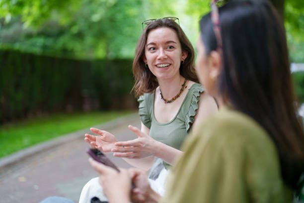 Young female adults hanging out together in a park, using mobile phones stock photo