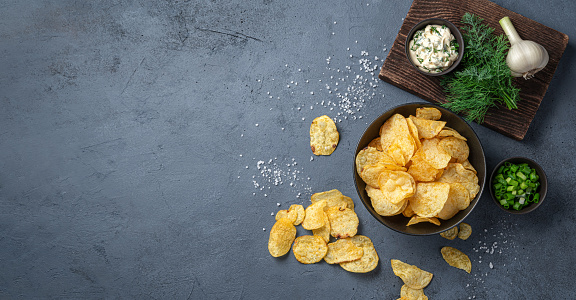 Crispy potato chips with herbs, salt and sour cream on a graphite background. Top view, copy space.