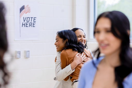 While voting at the community center, the young adult female friends embrace one another before leaving.