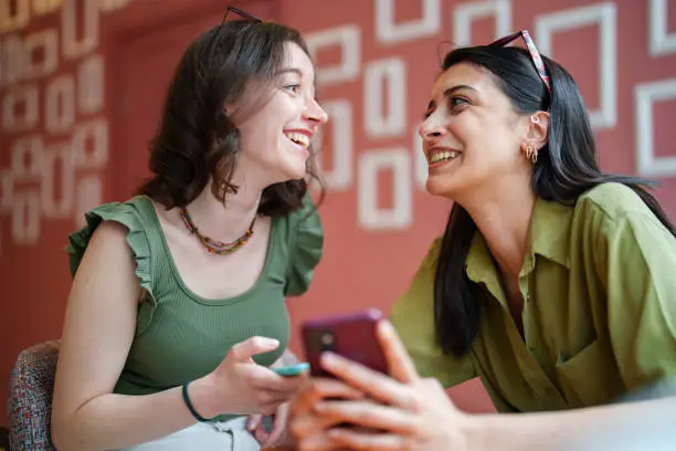 Photo of Young female adults meets at coffee shop, using mobile devices