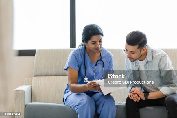 Young Man And Female Doctor Review The Medical Chart Together Stock Photo - Download Image Now