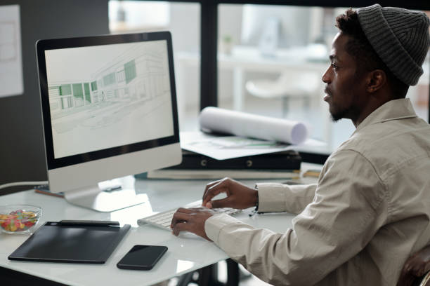 istock Young black man in casualwear looking at graphic sketches on computer screen 1500042182