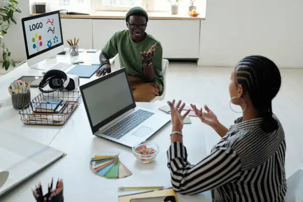 Young African American male webdesigner talking to confident female colleague explaining her viewpoint about creating new website