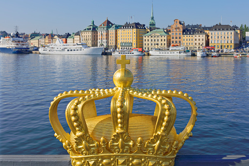 daytime view of the decorative gold crown on Skeppsholm bridge and the skyline of Gamla Stan (Stockholm, Sweden).