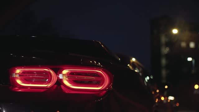 Black sports car tail light glowing in the dark of a night city