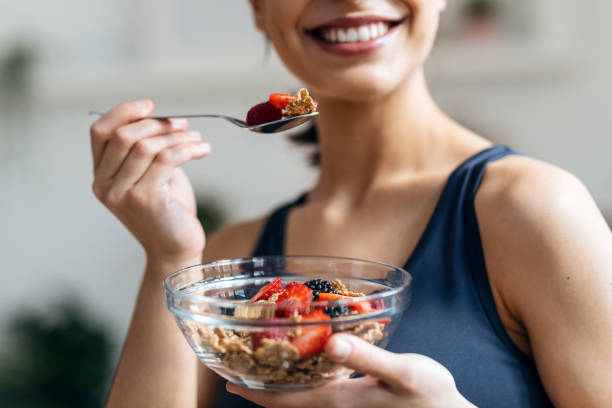 sportliche frau isst zu hause in der küche eine gesunde schüssel müsli mit obst - superfood stock-fotos und bilder