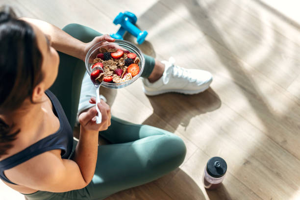 自宅の台所の床に座って果物とミューズリーの健康的なボウルを食べる運動女性 - sport food exercising eating ストックフォトと画像