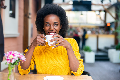 Portrait of beautiful smiling african-american woman sitting in urban cafe and drinking coffee.