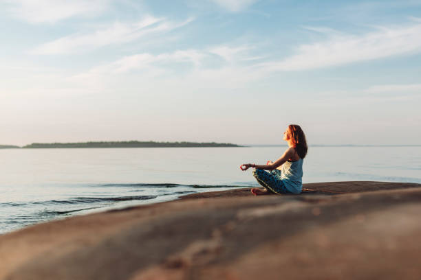 Young adult woman meditating at lake shore at sunset stock photo
