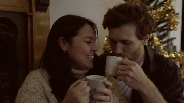 Christmas, coffee and funny couple in home laughing at comedy, humor and bonding. Tea, xmas and happy man and woman on holiday, relax and drinking beverage, love and enjoying quality time together.