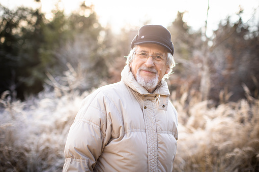 Happy senior man walking outside. Portrait of senior man in a forest on a winter day.