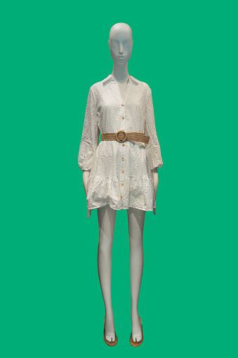 Full length image of a female display mannequin wearing trendy shirtdress with wicker belt isolated on green background