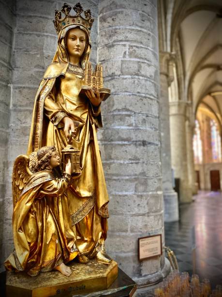 jeden naturalnej wielkości złoty posąg św. guduli stoi wzdłuż nawy katedry św. michała i św. guduli w brukseli w belgii. - st michaels church zdjęcia i obrazy z banku zdjęć