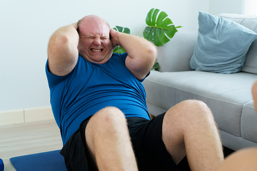 Very large body size - obese caucasian man doing a sit up on the floor, caucasian white fat or overweight man practicing and abs - sit up workout at home to improve his body shape and to be a better heath.