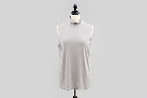 A gray short sleeve shirt hanging on a white headless mannequin isolated on a gray backdrop