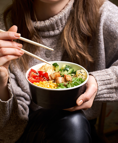 Clean eating diet concept. Chicken bowl with avocado in take out paper container in hands of woman having a lunch break. Close up.