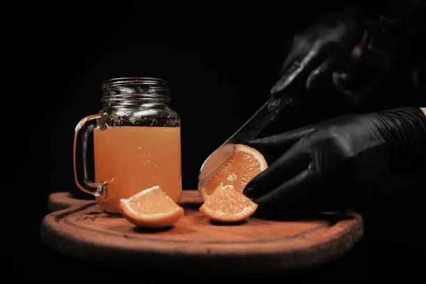 A chef slicing an orange into sections next to a glass