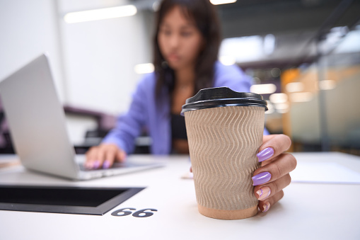Female worker holding cup of coffee on blurred background of open space office