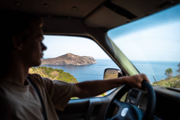 An adult boy driving a van, and through his window you can see a Mediterranean landscape.