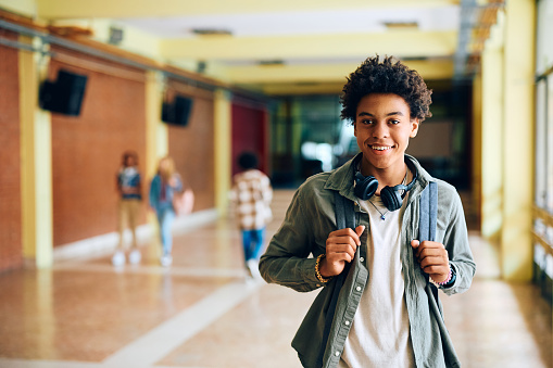 Happy African American high school student standing in hallway and looking at camera.