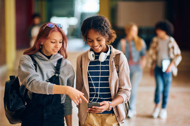 istock Happy black high school student and her friend using cell phone while walking through hallway at school. 1500076696