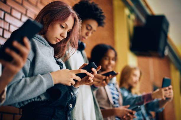 Group of teenagers using mobile phones in hallway at high school. High school student and her friends using their smart phones in a hallway. digital native stock pictures, royalty-free photos & images