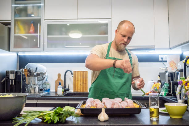 a blond man with a beard and a green apron prepares dinner in his home kitchen. - routine foods and drinks clothing household equipment imagens e fotografias de stock