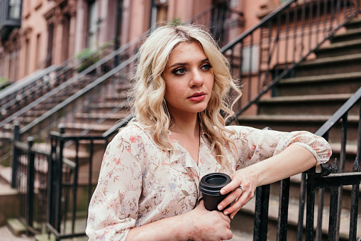 Elegant young woman waiting in the street enjoying a cup of coffee from a black cup.