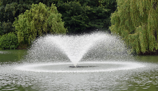 Chelmsford, Essex, United Kingdom, June 20, 2023. Fountains in the ornamental lake at Central Park, spraying and splashing water droplets in a circle. City centre public Central Park on summer day outdoors