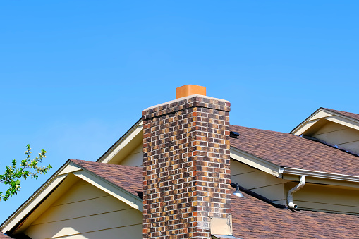 Chimney fireplace roof house ventilation against blue sky and blooming spring tree background with copy space. Landscape photo. Home repair or maintenance concept. Springt season. Architecture element