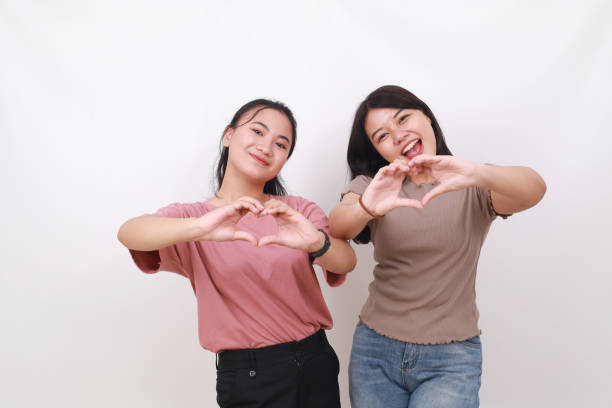 istock Two cheerful asian women standing while making love hand gesture. Isolated on white background 1500083187
