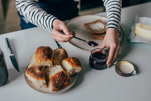 A close up view of an unrecognizable Caucasian female taking some homemade jam while preparing a sweet, tasty snack.