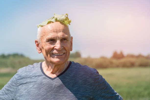 Old happy man with green leaf on head for sunstroke protect during sport exercising on hot summer day outdoor