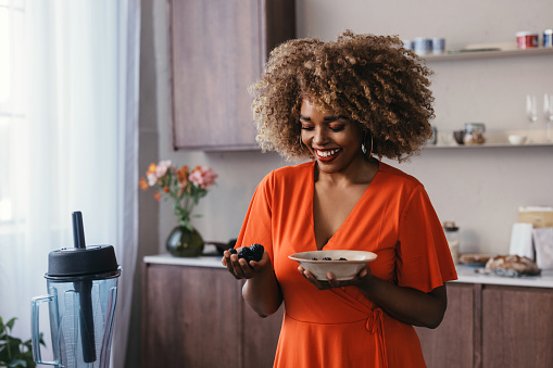 A happy African American woman standing in the kitchen, holding a bowl of blackberries.