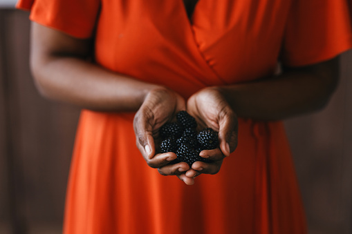 Unrecognizable African American Woman in an Orange Dress Holding Blackberries in her Hands