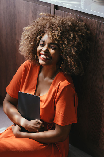 A happy African American woman in an orange dress sitting on the floor and using a digital tablet.