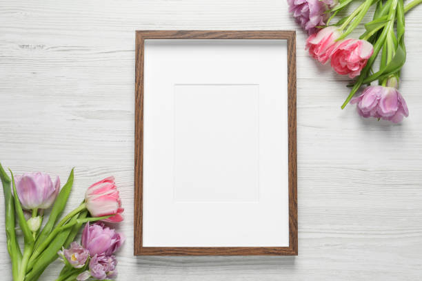 istock Empty photo frame and beautiful flowers on white wooden table, flat lay. Space for design 1500091276
