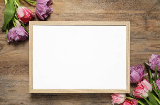 istock Empty photo frame and beautiful flowers on wooden table, flat lay. Space for design 1500091280