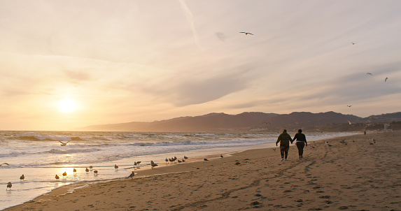 Two African American women walking along the shore in Santa Monica Beach, California, at sunset.